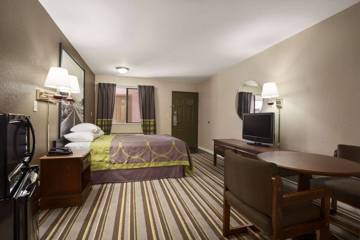 Ein Hotelzimmer mit einem Bett, einem Schreibtisch mit Fernseher, einem Sessel, einer Schreibtischlampe, einem Telefon und einem Spiegel.
