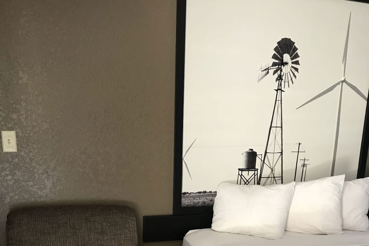 Ein Hotelzimmer mit Bett, Stuhl, kleinem Tisch und großem Fenster mit Blick auf eine Windmühle.