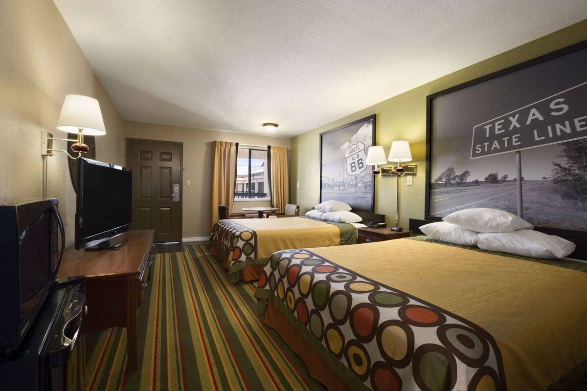 Ein Hotelzimmer mit zwei Betten, einem Fernseher, einem Schreibtisch und einem Fenster mit Vorhängen.