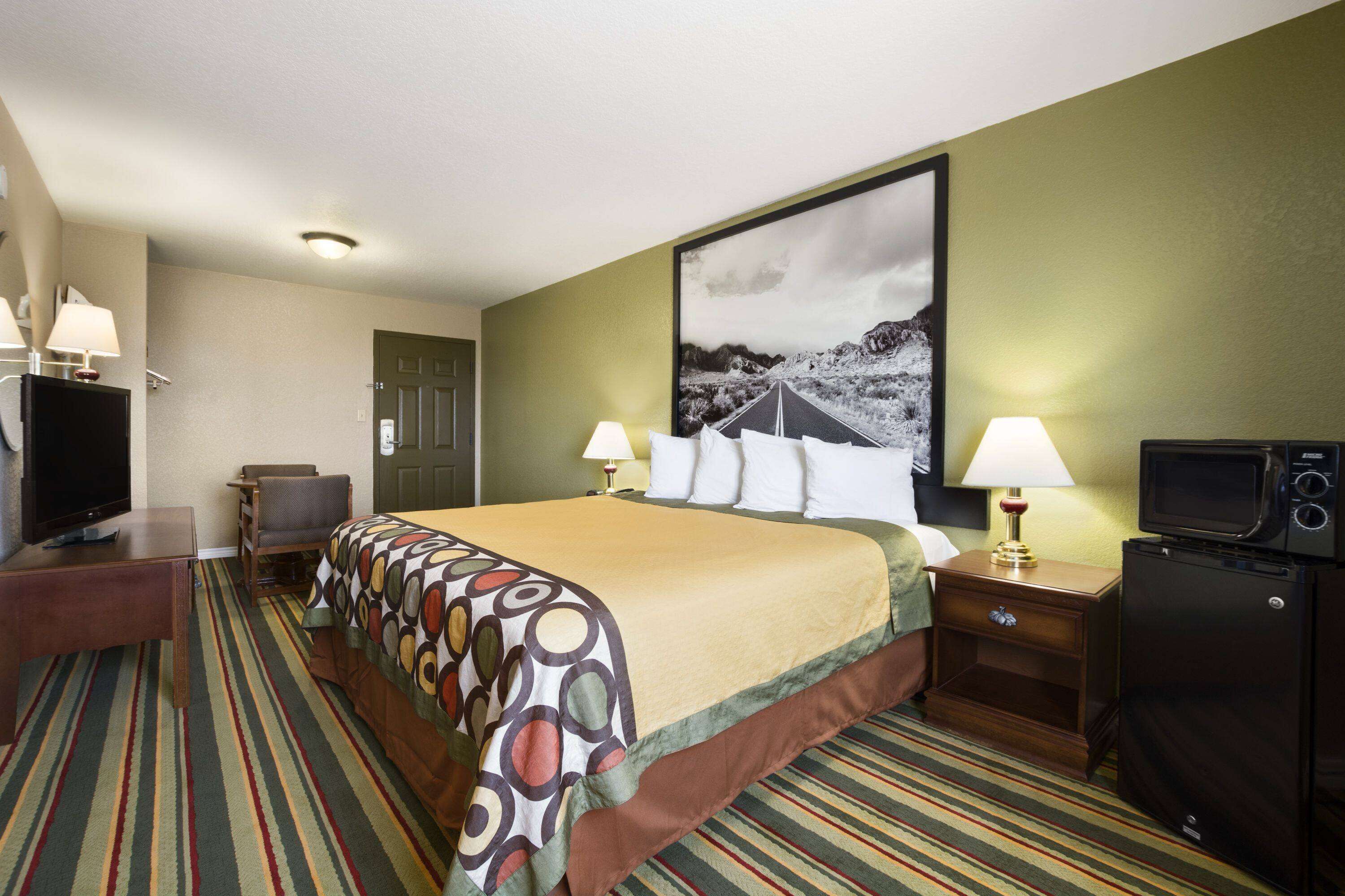 Ein Hotelzimmer mit Bett, Schreibtisch mit Fernseher, Sessel, Nachttisch mit Lampe und Mikrowelle.