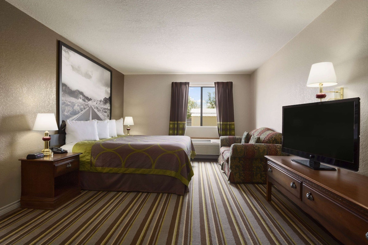 Ein Hotelzimmer mit Bett, Fernseher, Schreibtisch, Stuhl und einem Fenster mit Vorhängen.