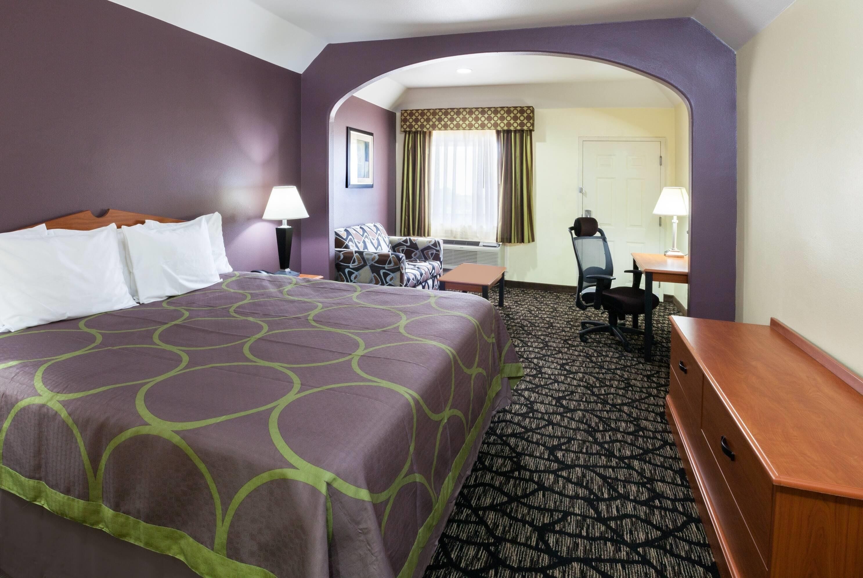 A hotel room with a large bed, a desk, a chair, and a small table.