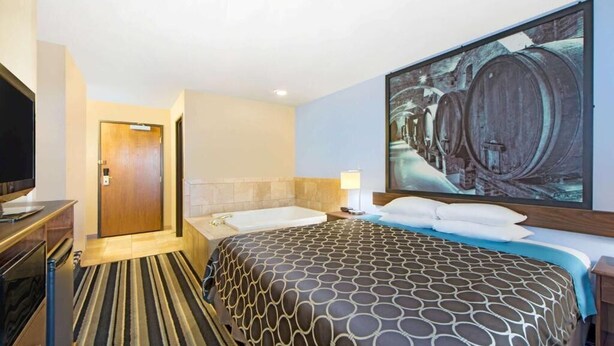 A hotel room with a large bed, a TV, a bathroom with a bathtub, and a painting of barrels on the wall.