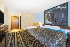 A hotel room with a large bed, a TV, a bathroom with a bathtub, and a painting of barrels on the wall. - Super 8 by Wyndham Fairfield Tx (Fairfield)