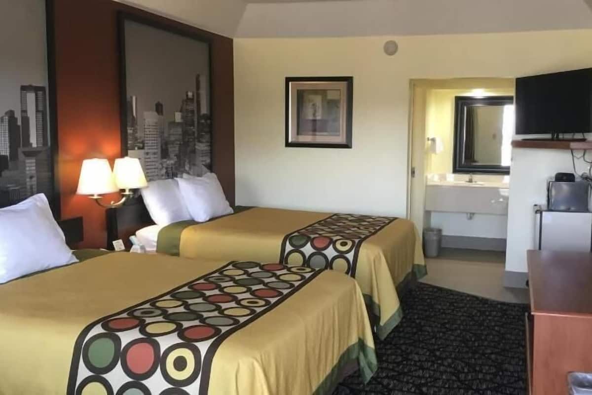 Hotelkamer met twee bedden, een bureau, een televisie, een spiegel en een badkamer die door een geopende deur zichtbaar is.