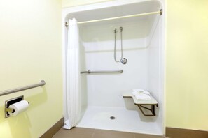 A handicap-accessible shower stall with a grab bar, a toilet paper dispenser, and a small shelf.