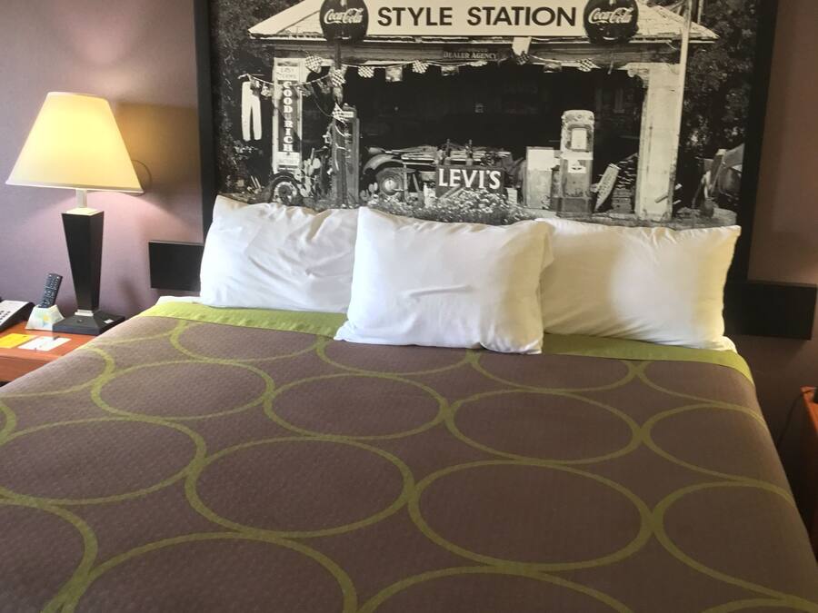 Una habitación de hotel con una cama y un edredón estampado con motivos geométricos, una fotografía en blanco y negro enmarcada de un restaurante antiguo en la pared, una lámpara en la mesita de noche y un control remoto.