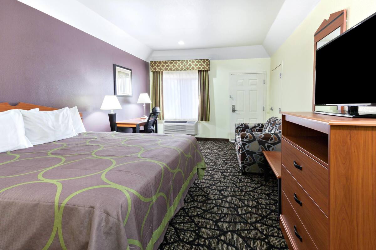 Een hotelkamer met een bed, een bureau met een lamp, een televisie, een dressoir en een kamerbreed tapijt met dessin.