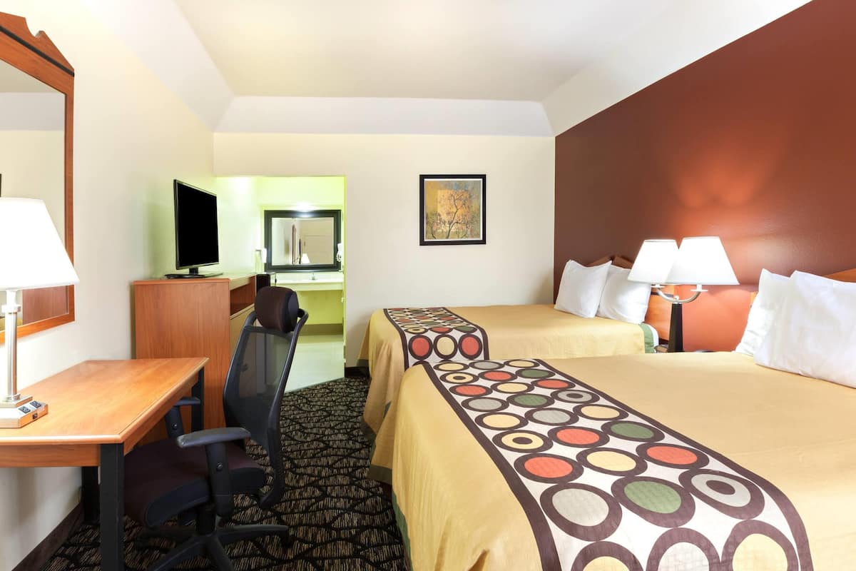 Een hotelkamer met een bureau, twee bedden, een stoel, een televisie en een spiegel.