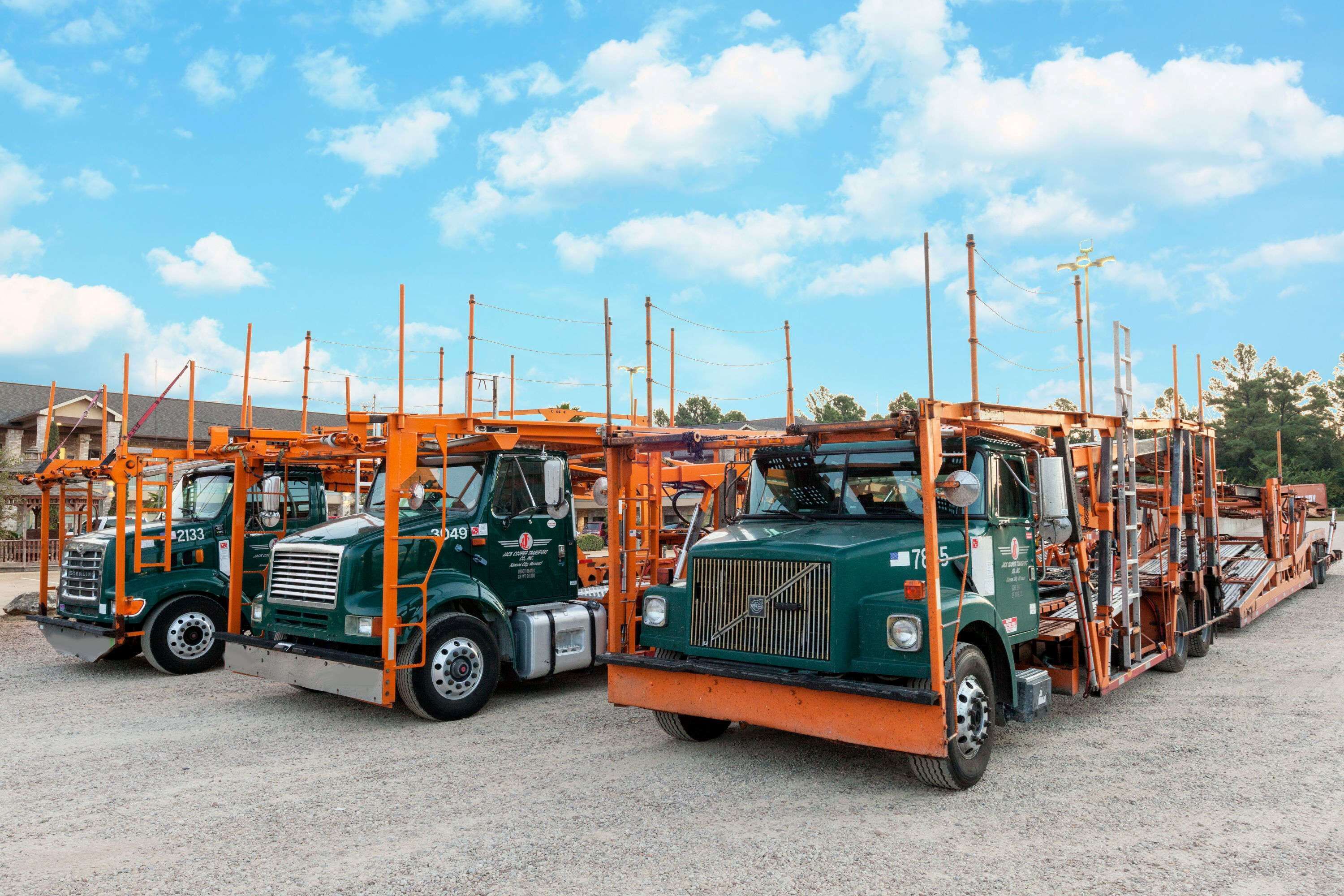 A row of green trucks with orange attachments parked in a gravel area.