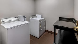A laundry room with a front-loading washer and dryer, a small table with a chair, and a tiled floor.