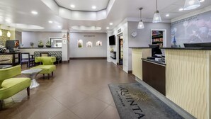 A hotel reception area with a modern design, including a reception desk, seating area with chairs, and a digital screen.