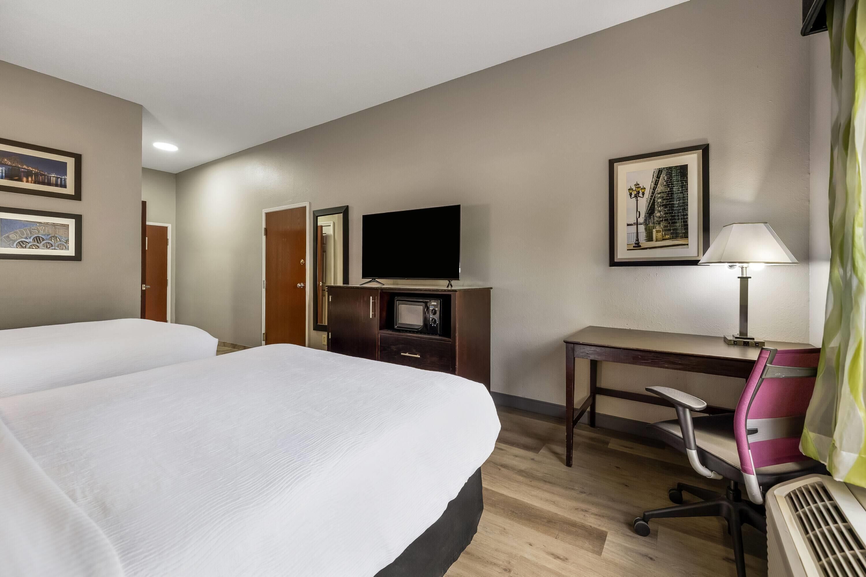 Una habitación de hotel con dos camas, un escritorio con silla, un televisor y una lámpara.