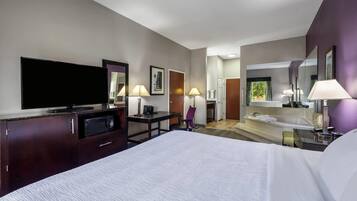A hotel room with a bed, a television, a desk with a lamp, a bathroom with a mirror, and a window.