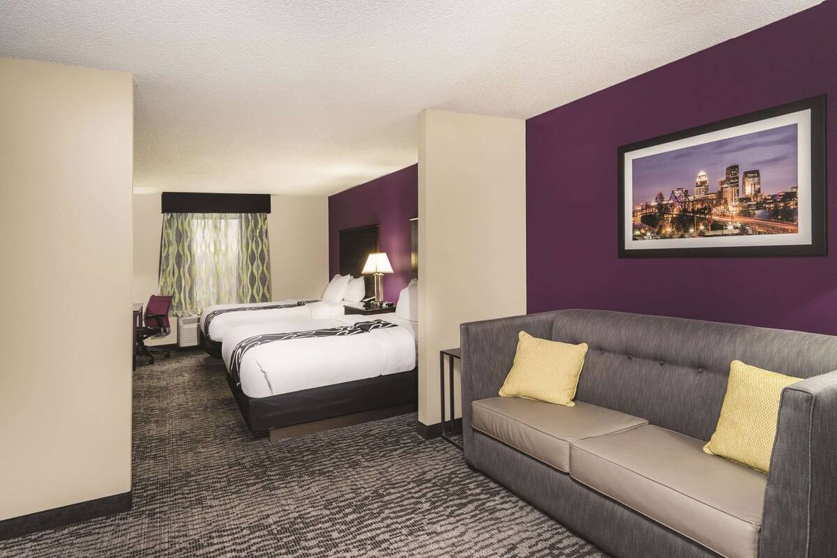 A hotel room with two beds, a sofa, a desk, and a cityscape painting.