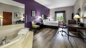 A hotel room with a bed, desk, chair, and a bathtub.