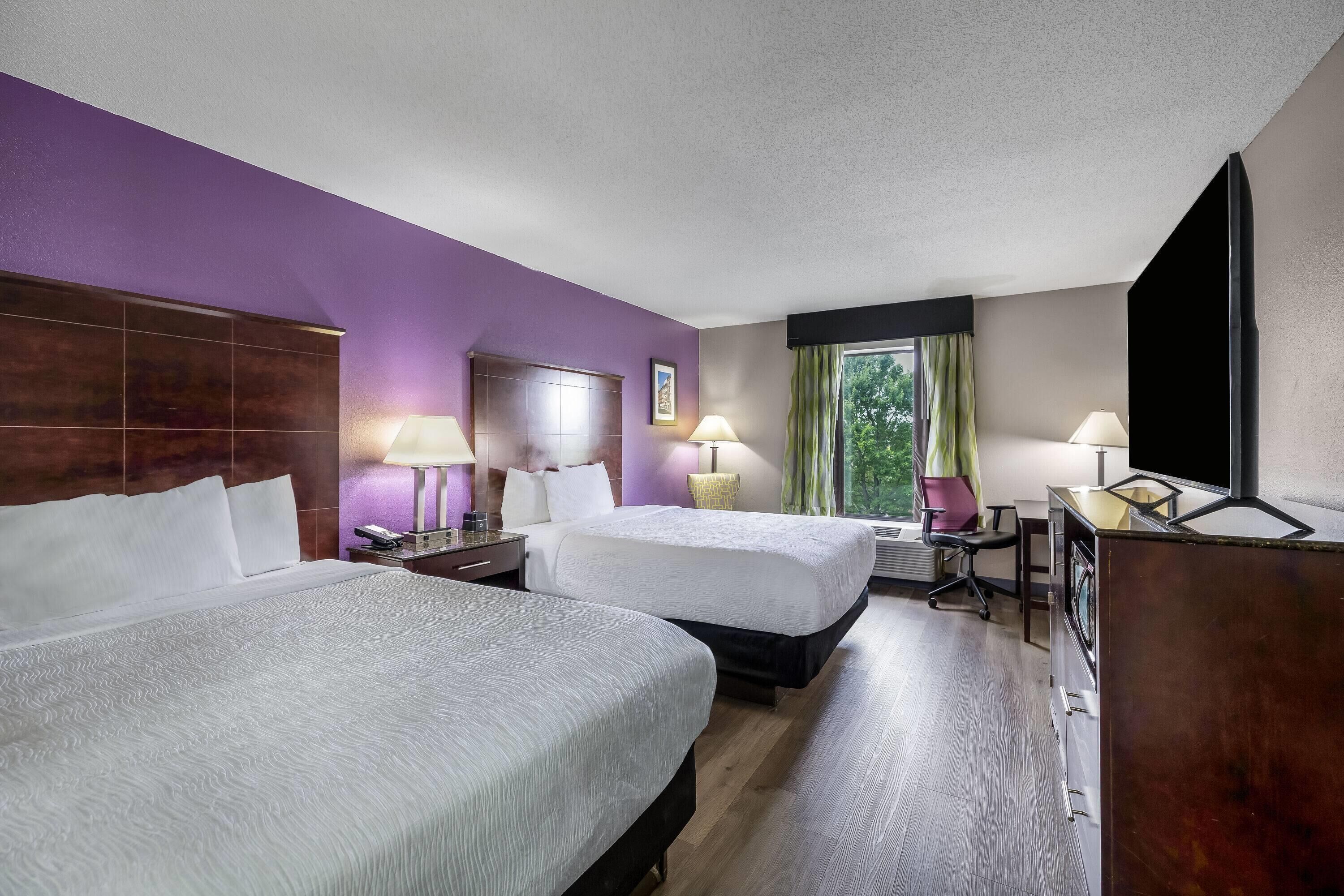 Habitación de hotel con dos camas, un escritorio, una silla, un televisor y una ventana con cortinas.