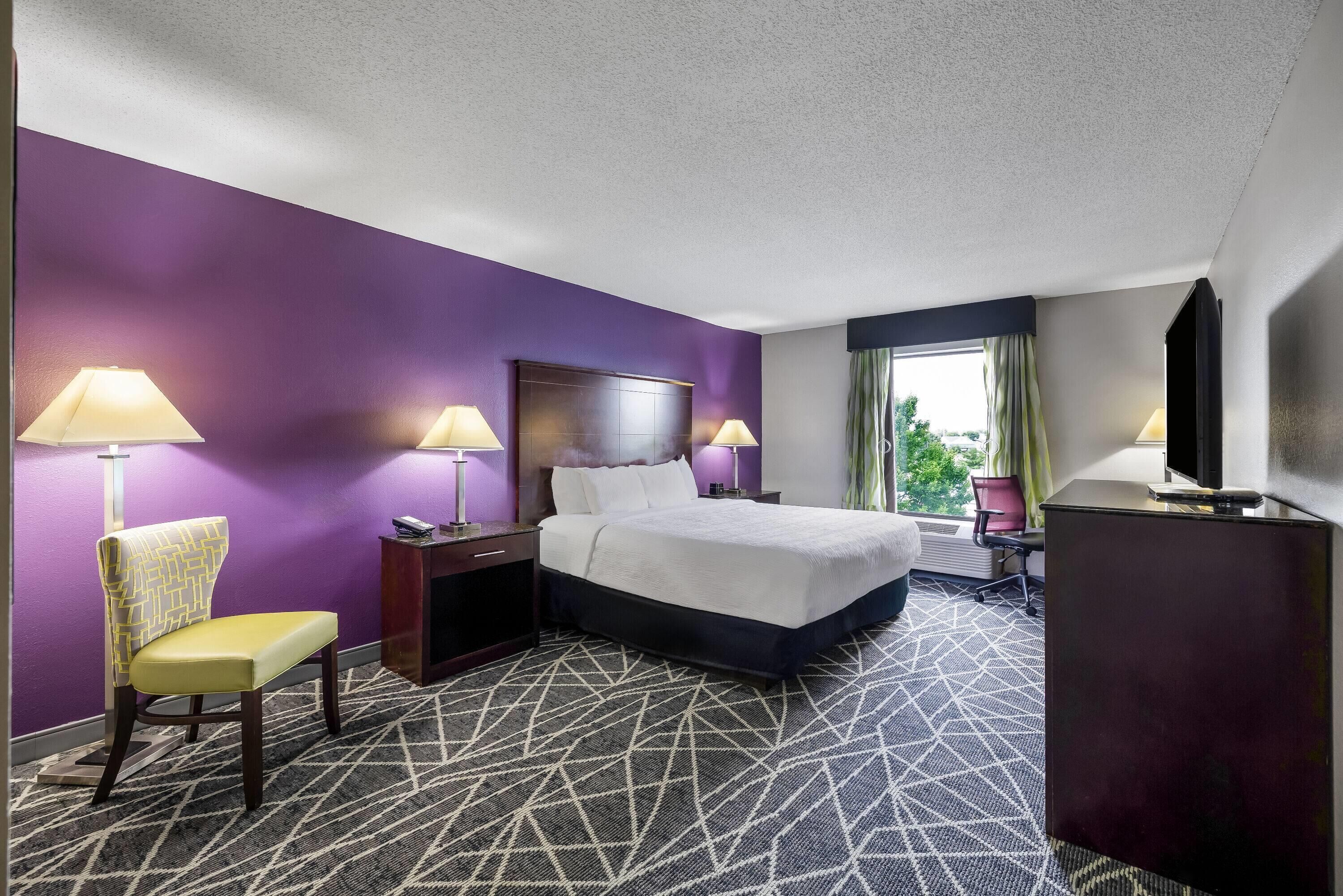 Une chambre d’hôtel comprenant un lit, deux tables de chevet, une chaise, un bureau et un téléviseur.