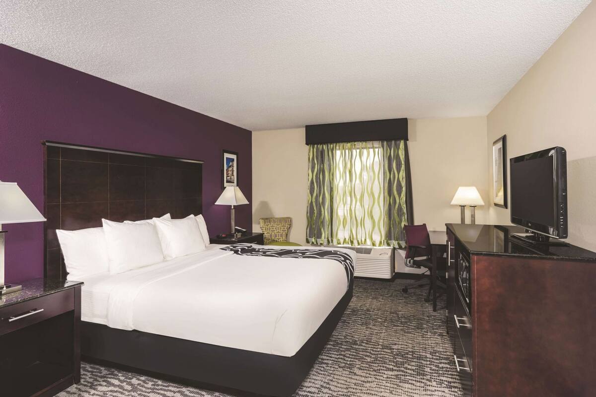 A hotel room with a large bed, a desk, a TV, and a window with curtains.
