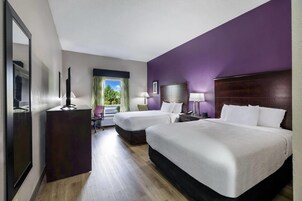 Habitación de hotel con dos camas, un escritorio, una silla, un espejo y un ventanal con cortinas.