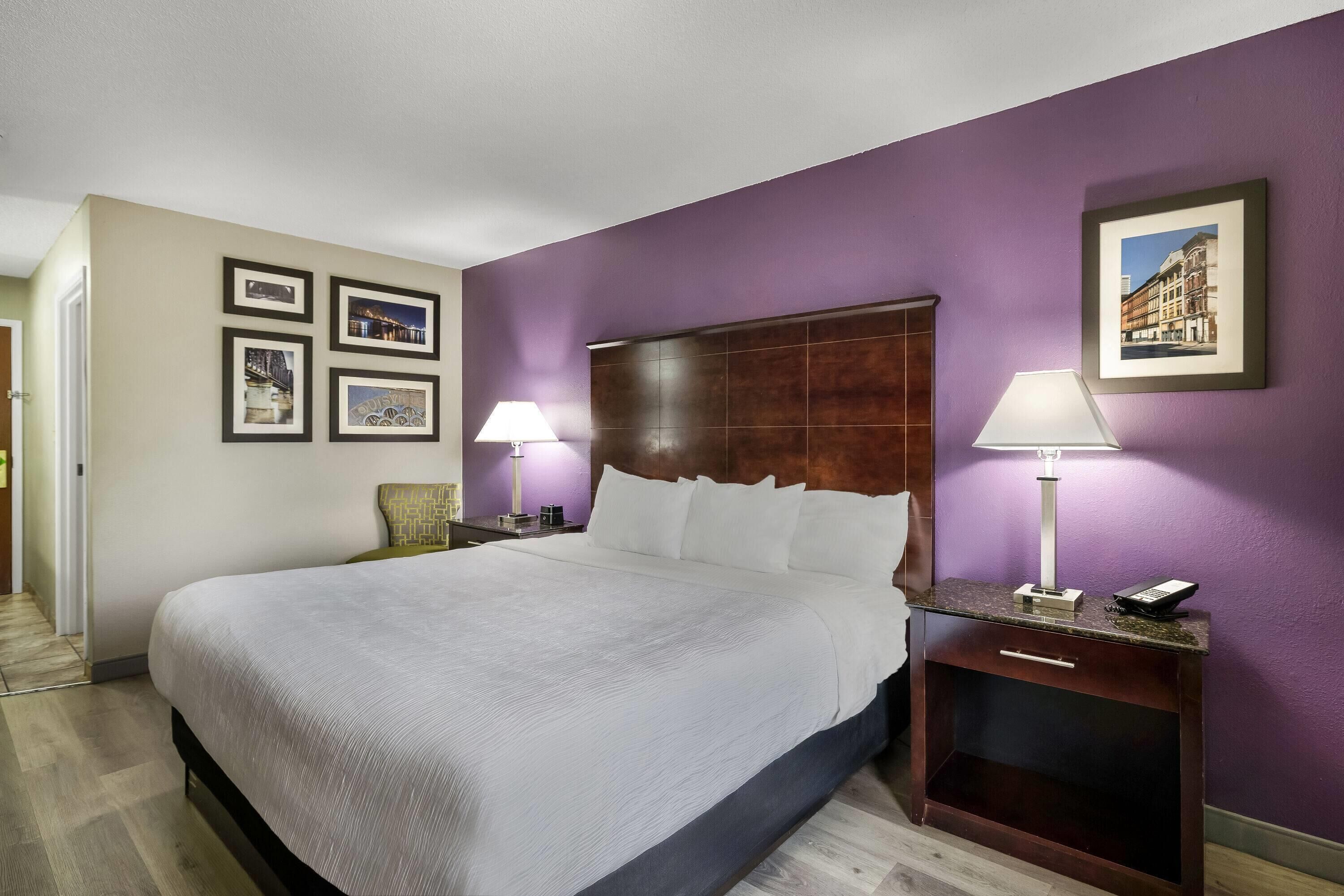 A hotel room with a large bed, two bedside tables with lamps, a wooden headboard, and framed pictures on the wall.