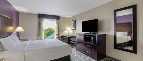 A hotel room with a bed, a desk, a television, and a large mirror.