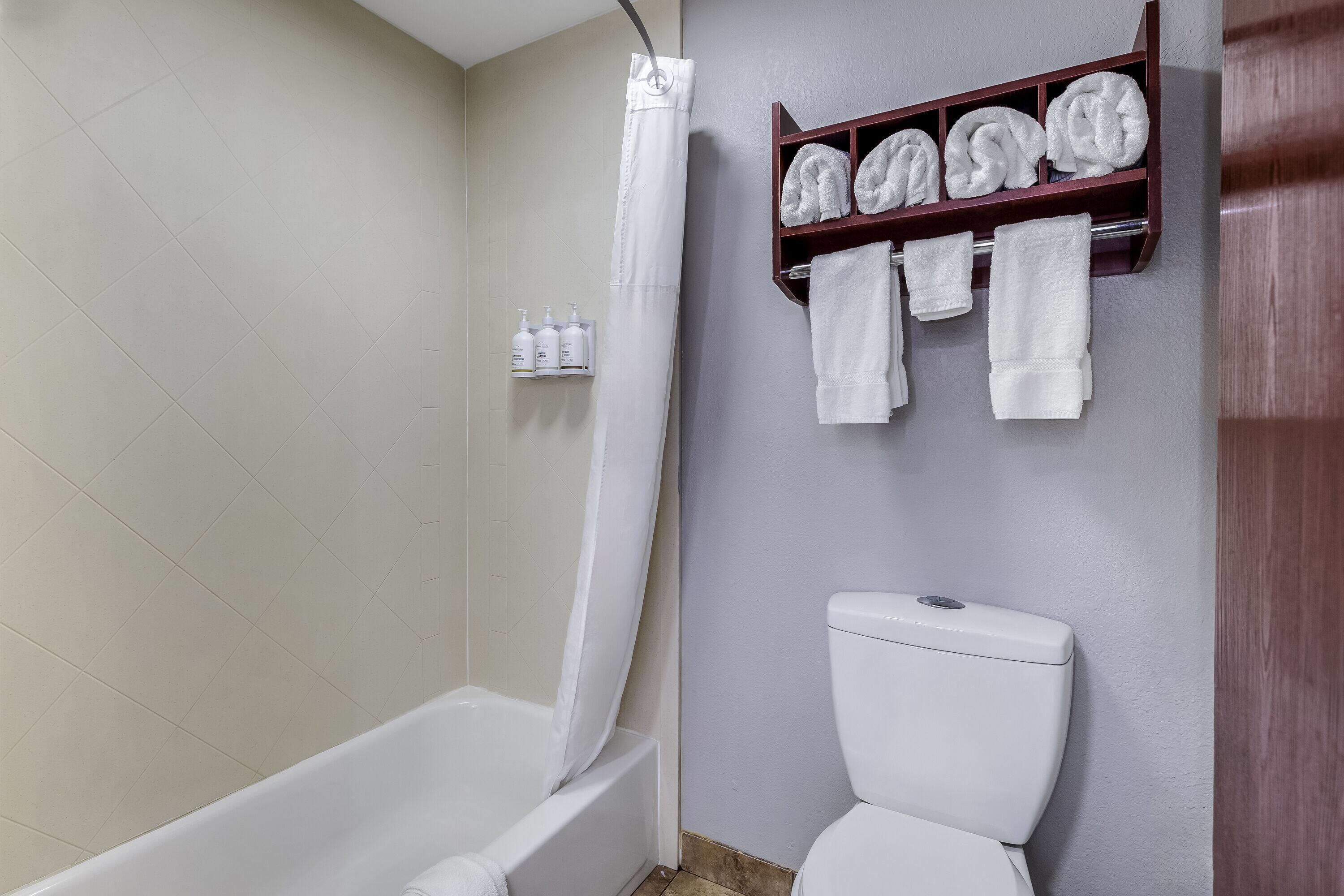 A bathroom with a bathtub, a toilet, and a shelf with towels.
