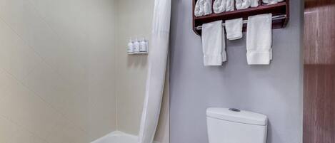 A bathroom with a bathtub, a toilet, and a shelf with towels.