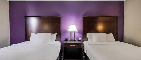 A hotel room with two beds, a nightstand with a lamp, and a wooden floor.