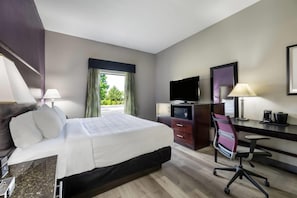 Una habitación de hotel con cama, escritorio, silla, televisor y ventana con cortinas.