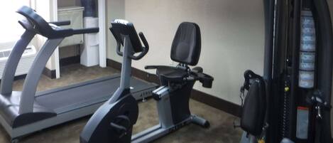Un gimnasio con cinta de correr, elíptica y banco para pesas.