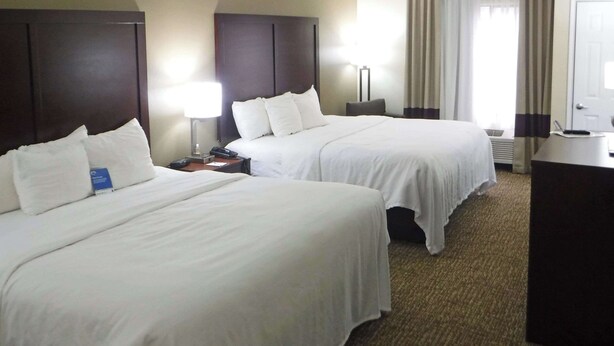 A hotel room with two beds, a desk, and a lamp.