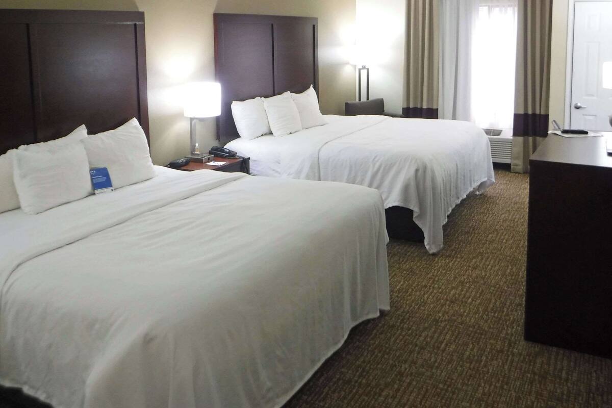 A hotel room with two beds, a desk, and a lamp.
