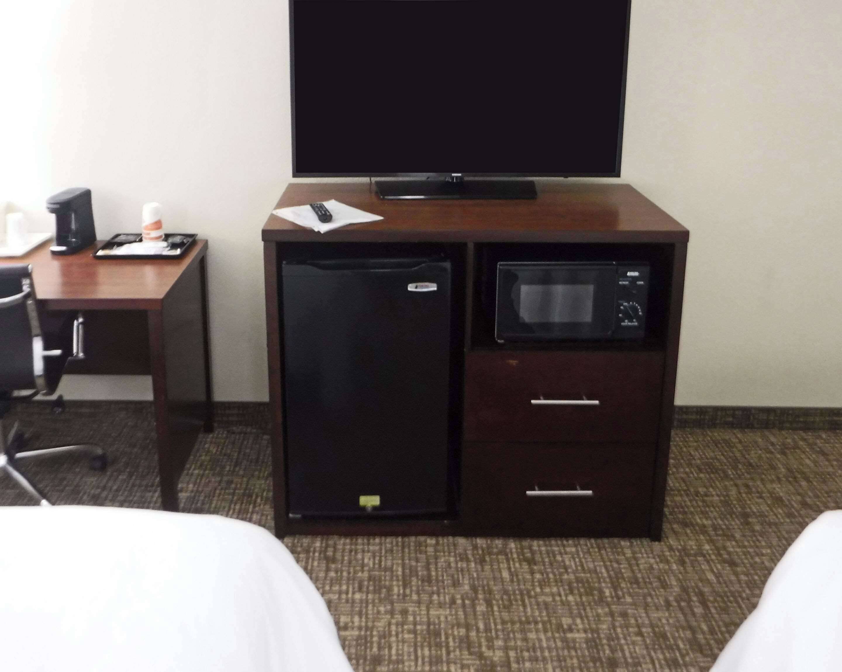 A compact hotel room with a bed, a desk with a computer, a refrigerator, and a microwave.