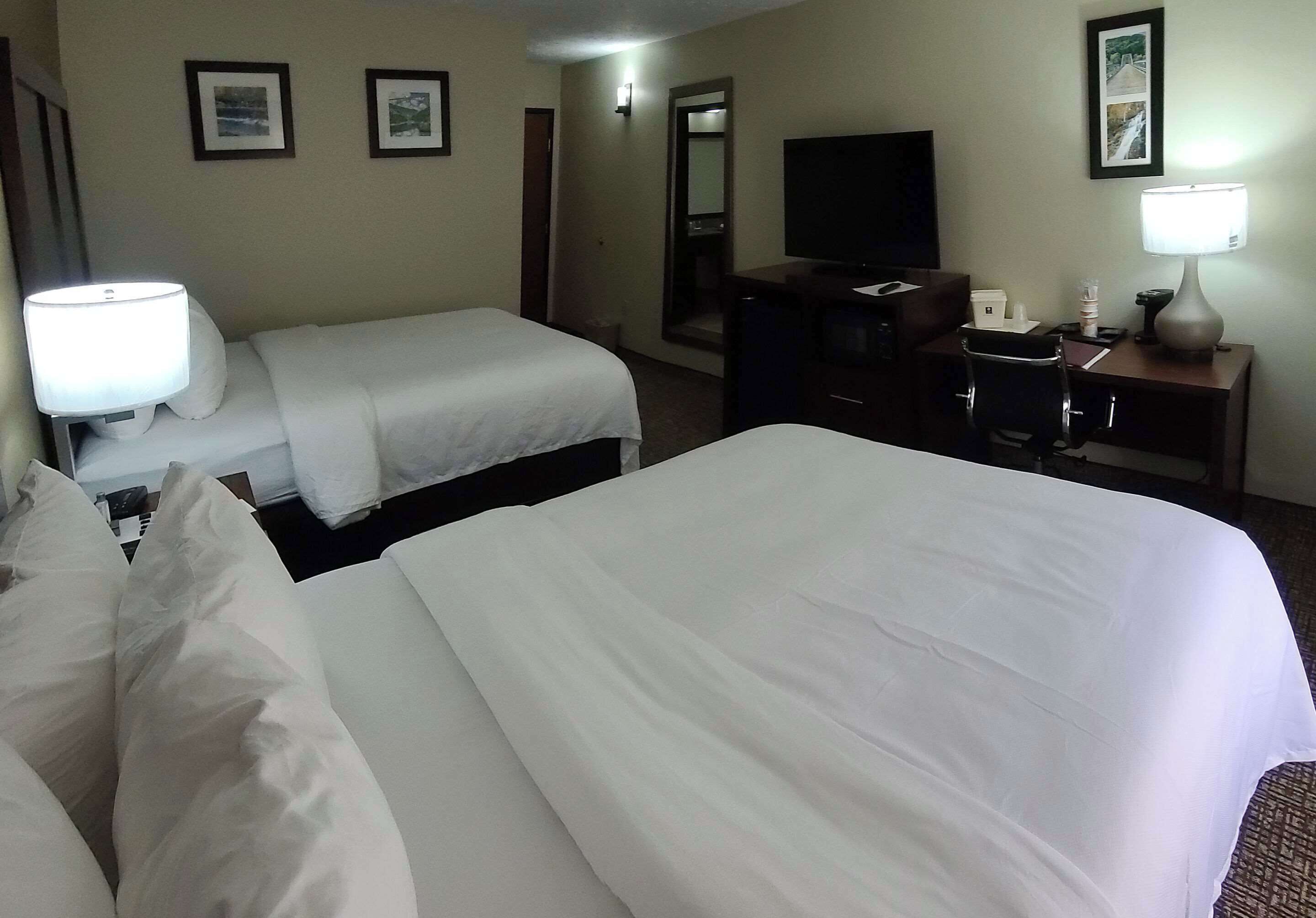 A hotel room with two beds, a desk with a lamp, a television, and framed pictures on the wall.