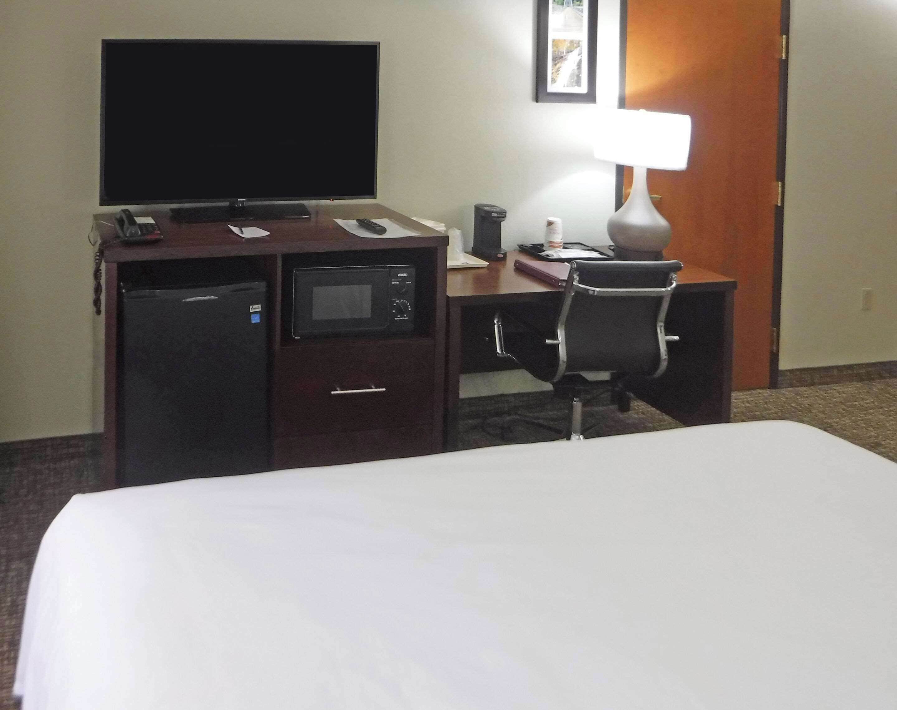 A hotel room with a bed, a desk with a computer, a TV, a microwave, and a lamp.