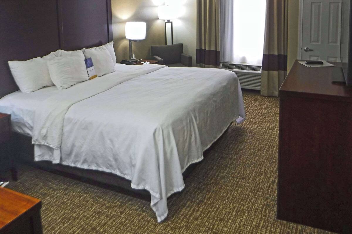 A hotel room with a large bed, a desk, a chair, a lamp, and a door.