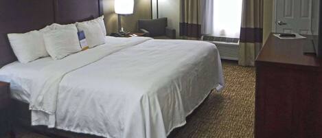 Habitación de hotel con una cama grande, un escritorio, una silla, una lámpara y una puerta.
