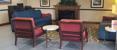 A lobby with a blue sofa, two wooden chairs, a small round table, a fireplace, and framed pictures on the walls.