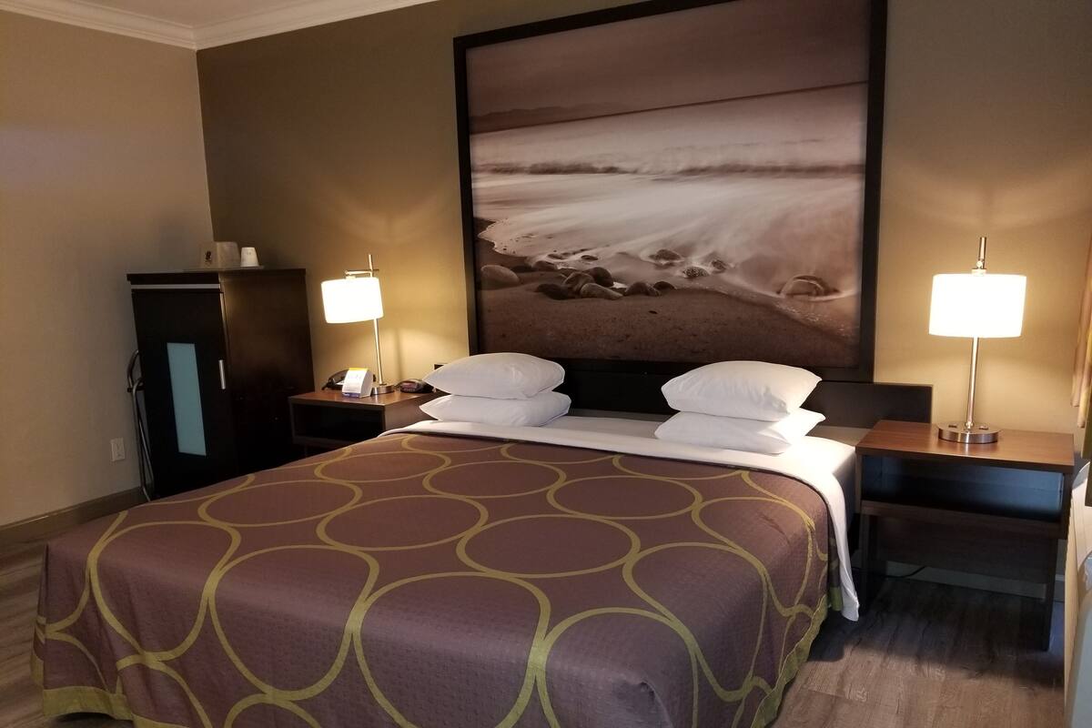 Une chambre d’hôtel avec un grand lit, deux tables de chevet avec des lampes, une table de nuit, une armoire et un grand tableau encadré au mur.