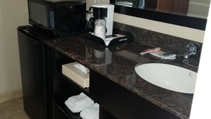 A compact hotel bathroom with a black countertop, a white sink, a microwave, a coffee maker, and a hairdryer. - Super 8 by Wyndham Los Angeles-Culver City Area (Los Angeles)