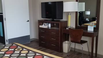 Habitación de hotel con una cama, un escritorio, un televisor, una silla, un espejo y un cesto de basura.