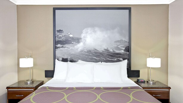 A hotel room with a bed, two nightstands, a large framed picture of a stormy sea, and a patterned bedspread. - Super 8 by Wyndham Los Angeles-Culver City Area (Los Angeles)