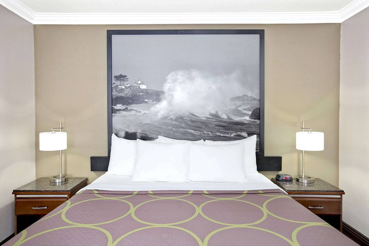 Une chambre d’hôtel avec un lit, deux tables de chevet, un grand tableau encadré représentant une mer déchaînée et une couvre-lit à motifs.