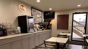 A breakfast area with a coffee machine, refrigerator, and a sign indicating hours of operation. There are tables and chairs for seating. - Super 8 by Wyndham Lafayette / Purdue Area (Lafayette)