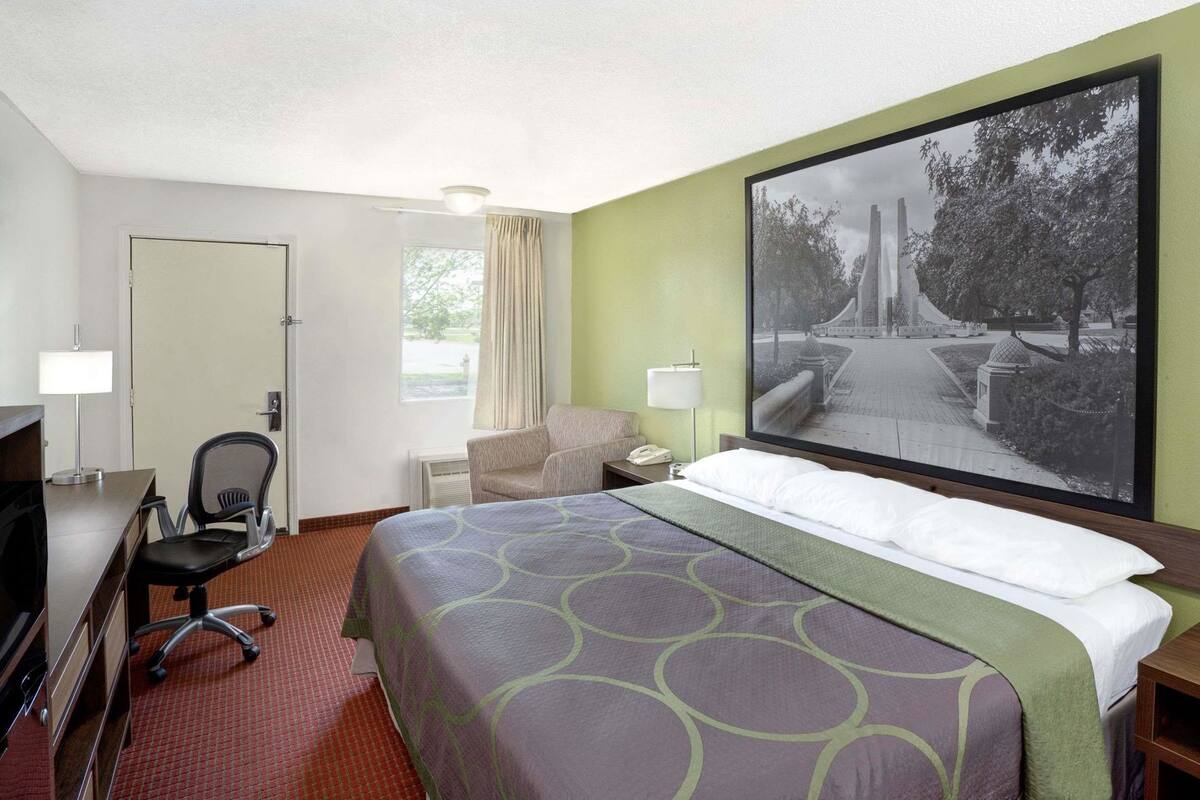 Une chambre d’hôtel avec un lit, un bureau, une chaise et un grand tableau encadré au mur.
