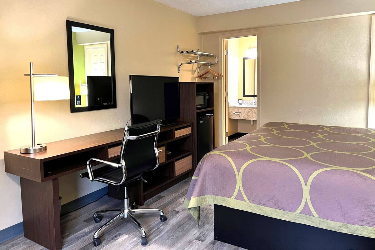 Une chambre d’hôtel équipée d’un bureau, d’une chaise, d’une télévision et d’un lit avec une couvre-lit à motifs.