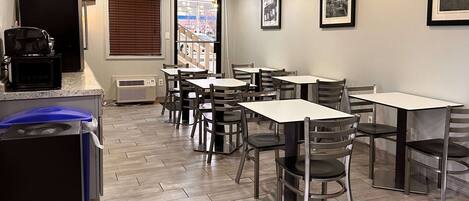 A clean, modern cafe with a herringbone floor pattern, multiple tables and chairs, a coffee machine, and framed pictures on the walls.