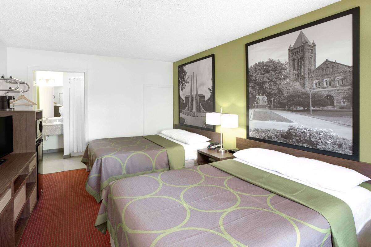 Une chambre d’hôtel avec deux lits, un bureau, une télévision et une salle de bain visible à travers une porte ouverte.