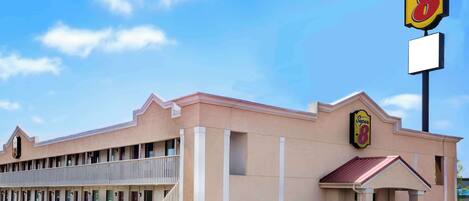 Um motel Super 8 com uma fileira de quartos, uma entrada coberta e um céu azul límpido.